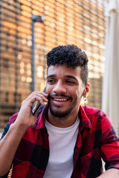 vertical portrait of young latin man talking on the phone happy and smiling, concept of technology and urban lifestyle - Zdjęcie, obraz