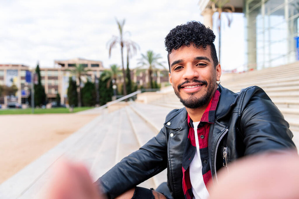selfie di un giovane latino che sorride felicemente in un parco cittadino, concetto di tecnologia e stile di vita urbano - Foto, immagini
