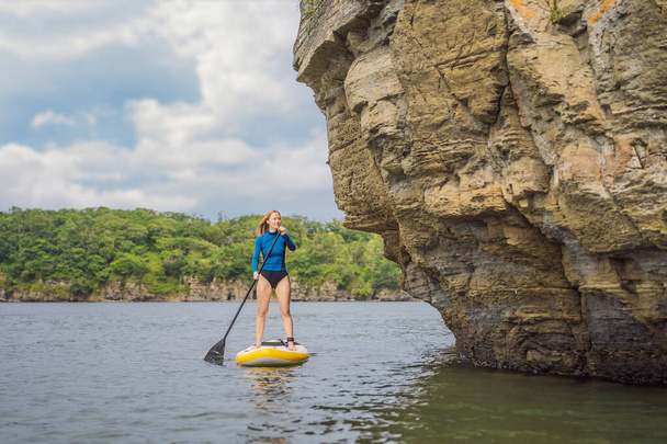Young women Having Fun Stand Up Paddling in the sea. SUP. Red hair girl Training on Paddle Board near the rocks - Foto, imagen