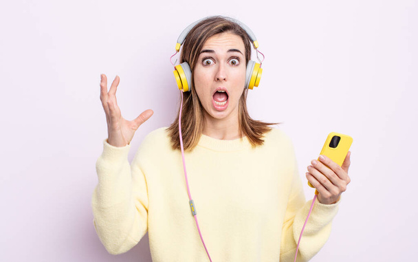 young pretty woman screaming with hands up in the air. headphones and phone concept - Photo, image
