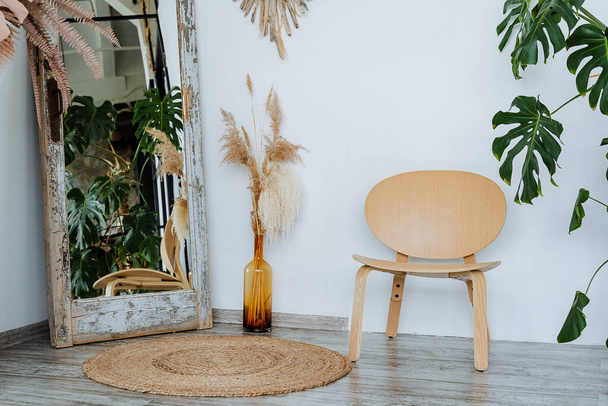 Interior shot. Bright room of the studio.A vase with piles of wheat Interesting wooden table. The main element of the room: a wicker mat. floor mirror and wooden chair. High quality photo - Foto, immagini