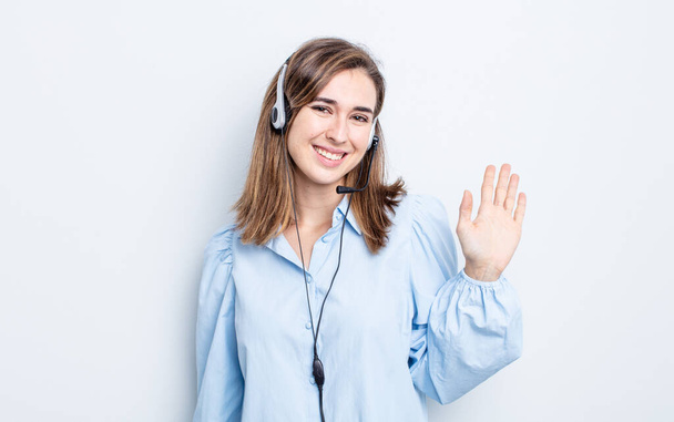 young pretty woman smiling happily, waving hand, welcoming and greeting you. telemarketer concept - Φωτογραφία, εικόνα