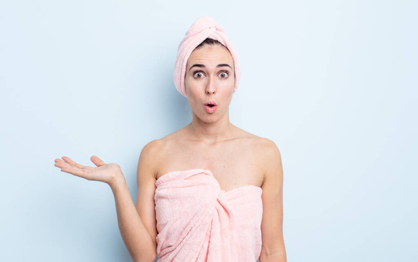 young pretty woman looking surprised and shocked, with jaw dropped holding an object. beauty and shower concept - Foto, Imagem