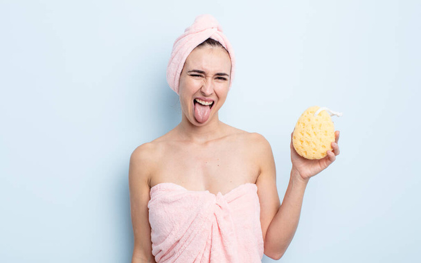 young pretty woman with cheerful and rebellious attitude, joking and sticking tongue out. shower and sponge concept - Photo, image