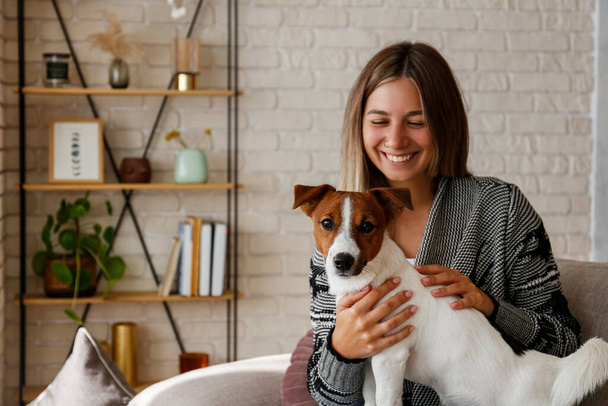 Portrait of young beautiful hipster woman playing with her adorable jack russell terrier puppy on the couch. Loving girl with her dog having fun. Background, close up, copy space - Φωτογραφία, εικόνα