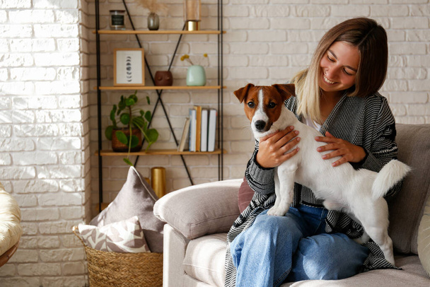 Portré fiatal gyönyörű hipster nő játszik az imádnivaló Jack Russell terrier kiskutya a kanapén. Szerető lány a kutyájával jól érzi magát. Háttér, közelről, másolás tér - Fotó, kép