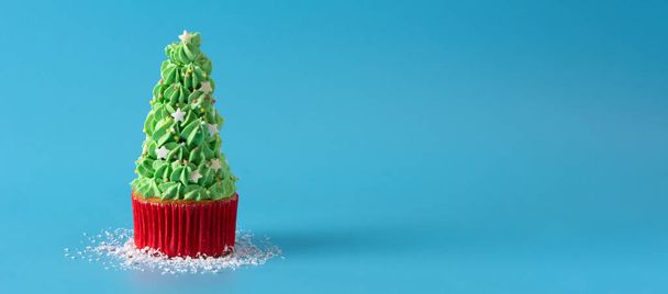 Snowing on Christmas tree cupcakes isolated on blue background.Panorama view - 写真・画像