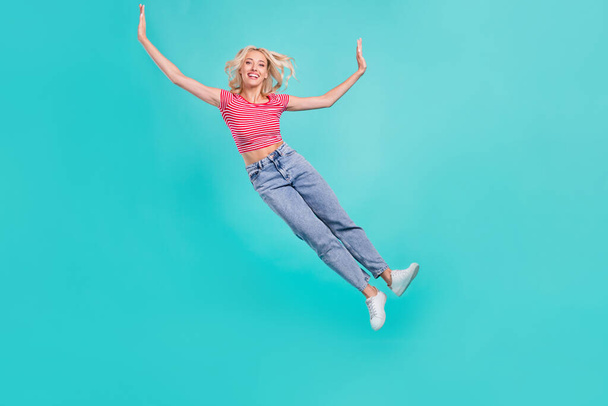 Photo of charming funky young lady wear striped t-shirt jumping high falling smiling isolated turquoise color background. - Foto, imagen