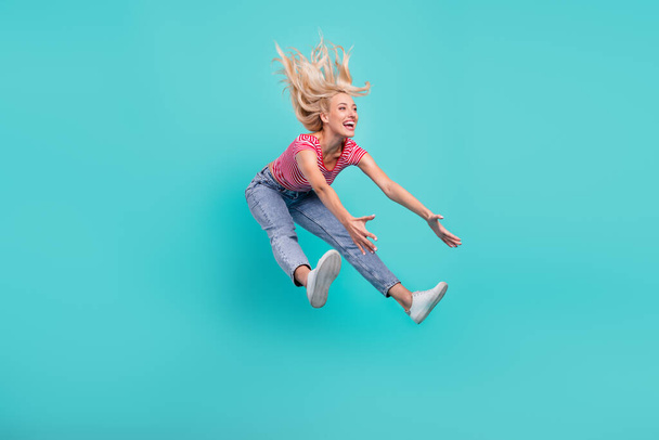 Photo of pretty funky young woman dressed red t-shirt smiling jumping high catching empty space isolated teal color background. - Φωτογραφία, εικόνα