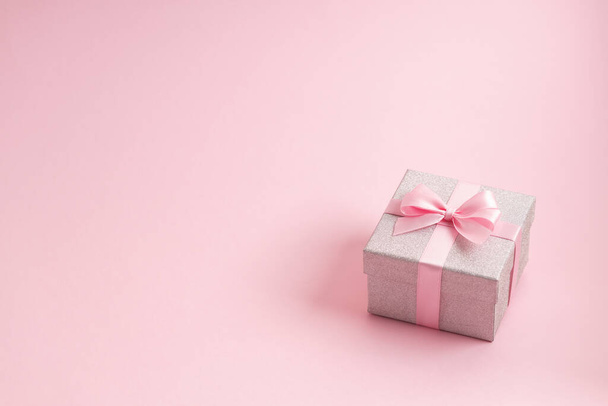 Ezüst csillogó ajándékdoboz rózsaszín szalaggal, rózsaszín háttérrel. Karácsony, Valentin-nap vagy születésnap koncepció. - Fotó, kép