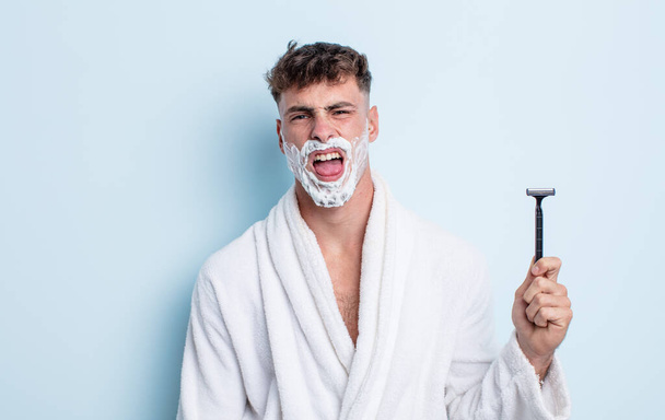 young handsome man feeling disgusted and irritated and tongue out. shaving concept - Foto, Imagen