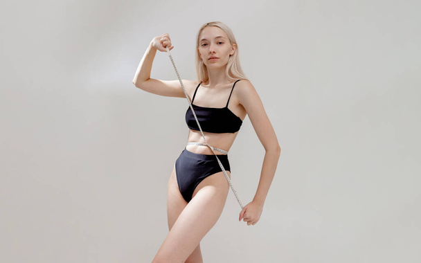 a slender girl in a swimsuit measures her waist with a centimeter - Photo, Image