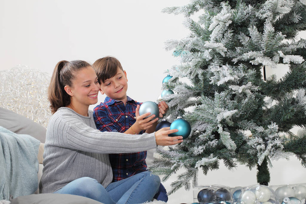 vrolijk kerstfeest familie thuis, glimlachende broer en zus versieren de boom hangen blauwe ballen zitten op de vloer in livong kamer - Foto, afbeelding