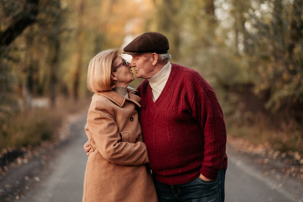 Homme âgé regarde avec amour sa pensionnée élégante, embrasse et jouit de sa beauté, couple marié senior dansant dans le parc d'automne, fête anniversaire, affection - Photo, image