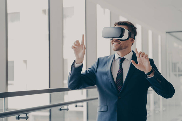 Handsome smiling businessman in vr headset using innovative technologies for business at work - Foto, afbeelding