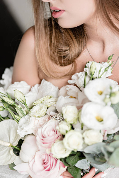 beautiful wedding bouquet in the hands of a charming bride.  Close-up of a brides bouquet in white-peach shades. The bride in a  white dress holds a bouquet in her hands. White sand. Close-up bunch of florets. Bridal accessories.  - Zdjęcie, obraz