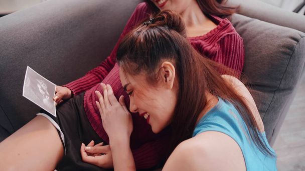 Happy pregnant lesbian couple looking ultrasound image together on sofa. - Foto, afbeelding