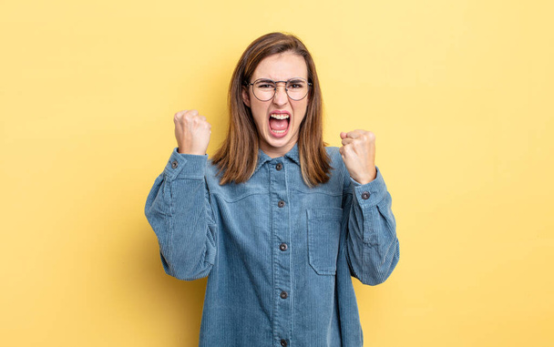 young pretty girl shouting aggressively with an angry expression or with fists clenched celebrating success - Foto, afbeelding