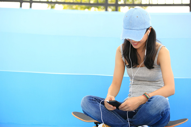 Woman skateboarder sit on skatepark stairs listening music from smart phone mp3 player - Photo, image
