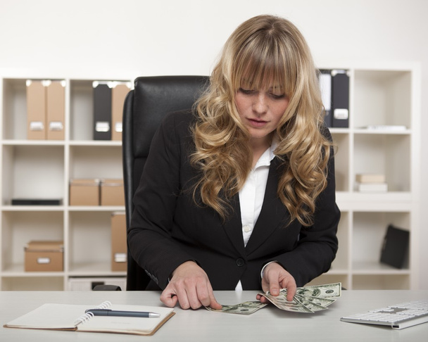 Businesswoman counting out money at her desk - Foto, Bild