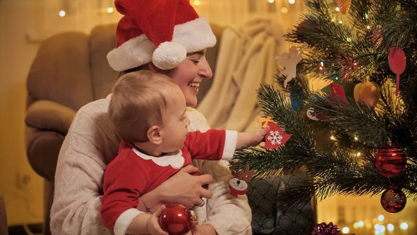 Petit garçon loooking sur l'arbre de Noël lumineux et enlever les boules de Noël. Familles et enfants célébrant les vacances d'hiver. - Photo, image