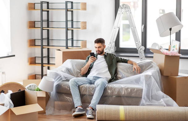 man with smartphone and boxes moving into new home - Valokuva, kuva
