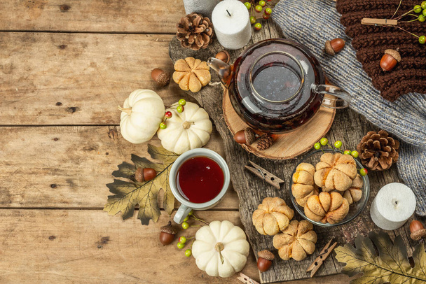 秋のお茶のコンセプト。カボチャのピューレとクッキー、ガラスティーポットの紅茶、秋の装飾。リースキャンドル居心地の良いセーター。古い木の背景、トップビュー - 写真・画像