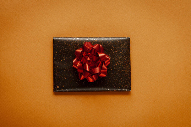 Dark present box with red bow on yellow background, top view - Valokuva, kuva
