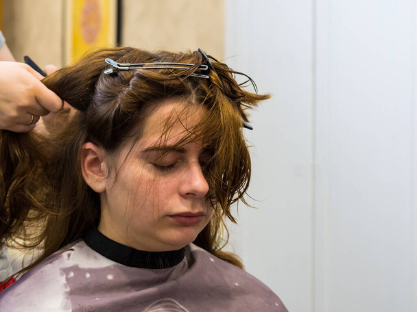 Nahaufnahme des Haarschnitts einer Frau. Schöne junge Brünette beim Friseur. Die Friseurin frisiert sich die Haare. - Foto, Bild