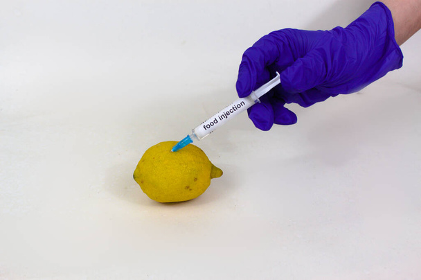 Ін'єкційний лимон крупним планом з шприцом для ін'єкцій їжі на рукавичках
 - Фото, зображення