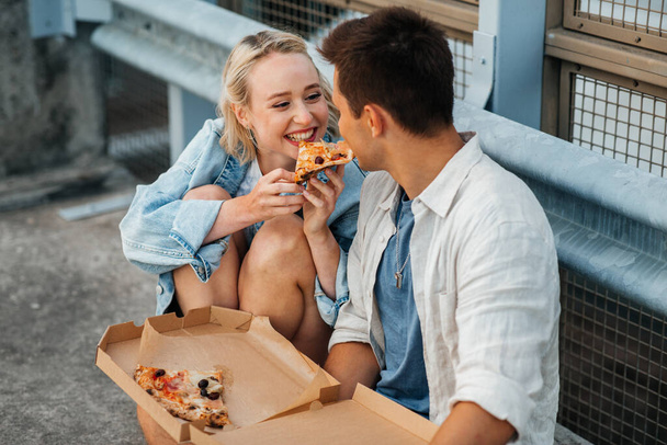 happy couple eating pizza on city roof top parking - Fotoğraf, Görsel