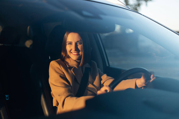View through the windshield at cheerful young woman sitting in the car - 写真・画像