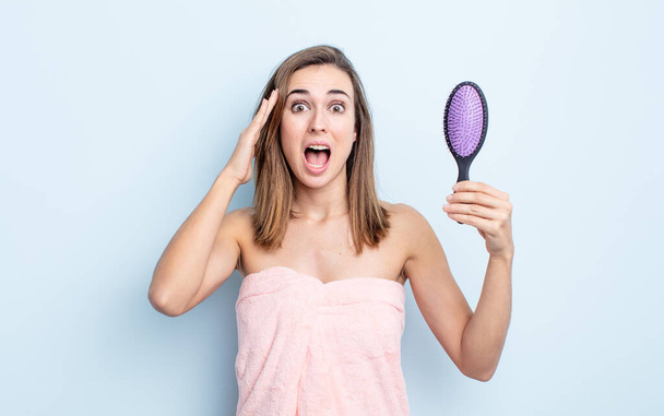 young pretty woman looking happy, astonished and surprised. hairbrush concept - Фото, изображение