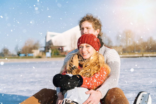 Любящая пара в теплых свитерах веселится на льду. Женщина и мужчина катаются на коньках на открытом воздухе в солнечный снежный день. Активное свидание на ледовой арене в зимний сочельник. Романтические мероприятия и концепция образа жизни. - Фото, изображение