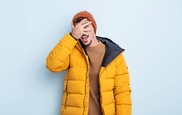 young handsome man looking shocked, scared or terrified, covering face with hand. winter concept - Φωτογραφία, εικόνα