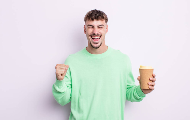 young handsome man feeling shocked,laughing and celebrating success. take away coffee concept - Fotó, kép