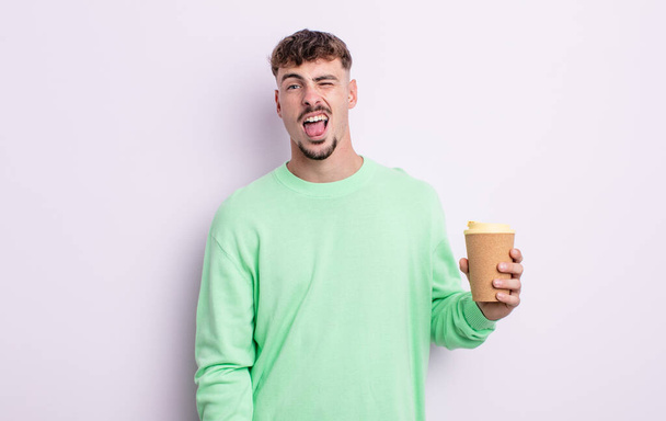 young handsome man with cheerful and rebellious attitude, joking and sticking tongue out. take away coffee concept - Foto, Imagem