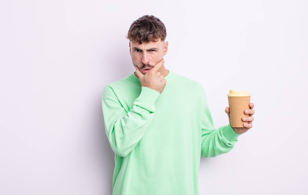 young handsome man with mouth and eyes wide open and hand on chin. take away coffee concept - Foto, Imagen