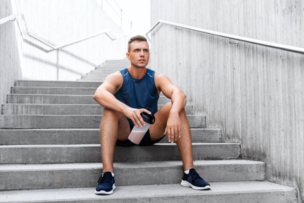 sportsman with shake in bottle sitting on stairs - Foto, Imagen