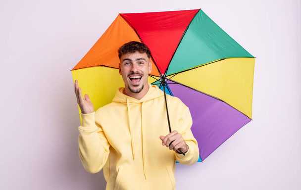 young handsome man feeling happy and astonished at something unbelievable. umbrella concept - Foto, Bild