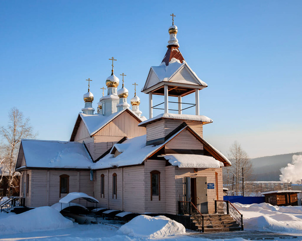 Blick auf das Holzgebäude der Kirche zu Ehren des Erlösers, der nicht mit Händen gemacht wurde, in der Stadt Ust-Kut an einem Wintertag. Kirche im Schnee bei minus 40 Grad Celsius im Dezember. Kälte, Sibirien, Russland.  - Foto, Bild