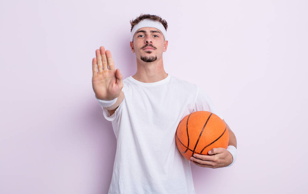 young handsome man looking serious showing open palm making stop gesture. basketball concept - Foto, immagini