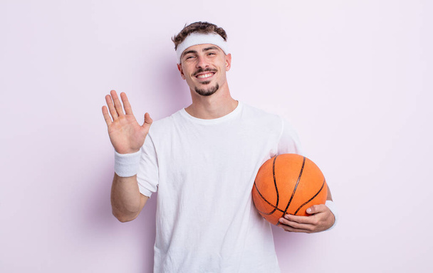 young handsome man smiling happily, waving hand, welcoming and greeting you. basketball concept - Foto, imagen
