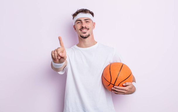 young handsome man smiling and looking friendly, showing number one. basketball concept - Foto, imagen