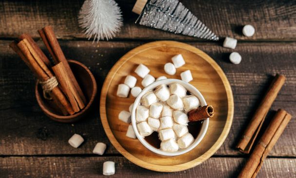 Top view  hot spicy drink with marshmallows on wooden background. Cinnamon sticks and  small Christmas tree  mess on table. - Fotó, kép