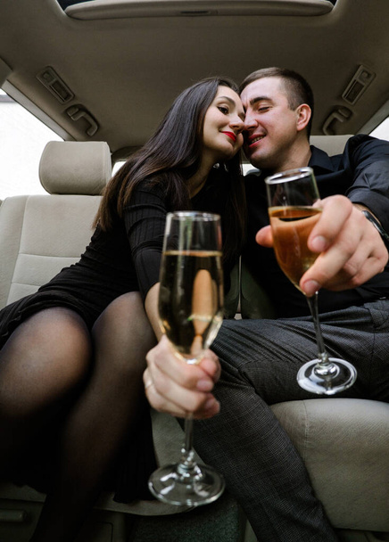 Happy young man and woman drinking champagne in car. - Фото, изображение