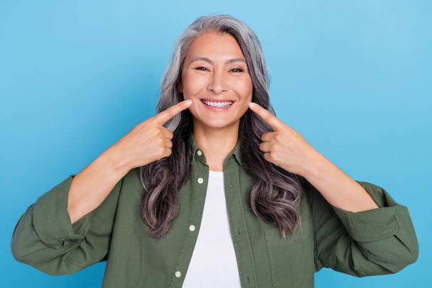 Photo of funny aged grey hairdo lady indicate teeth wear khaki shirt isolated on blue color background - Foto, immagini