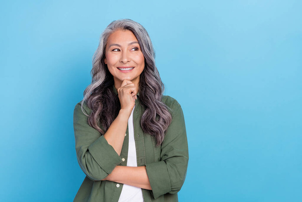 Photo of thinking aged grey hairdo lady look empty space wear khaki shirt isolated on blue color background. - Foto, Imagen