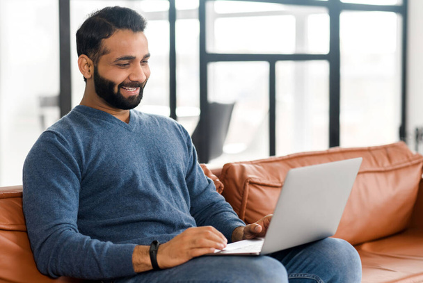 Cheerful Indian man wearing casual wear sitting on the sofa and using laptop - Foto, immagini