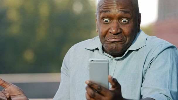 Божевільний стресовий африканський чоловік тримає мобільний телефон роздратований повідомленням про помилку мобільного додатку на повільному застряглому розбитому смартфоні, сердитий чорний чоловік розчарований проблемою телефону, маючи скарги на погану службу
 - Фото, зображення